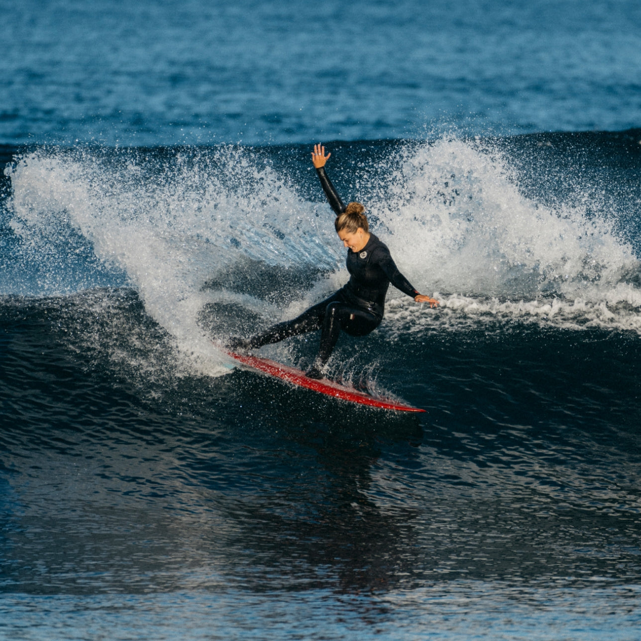 Woman surfing on a wave with a black wetsuit and red surfboard.
