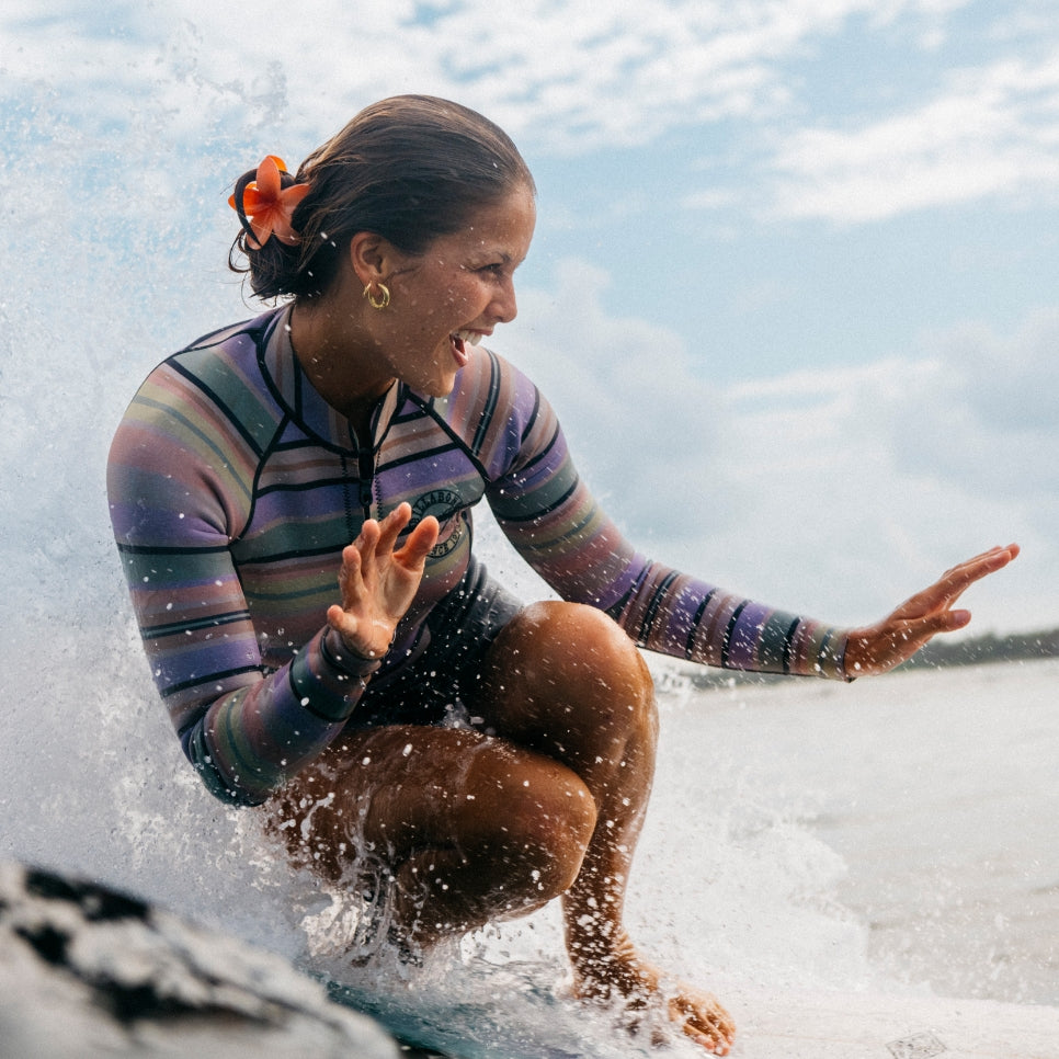 A woman in a lively springsuit on a wave, capturing the excitement of surfing in sunny coastal setting.